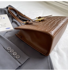 Detail of brown crocodile embossed leather tote bag with elegant golden metallic buckle