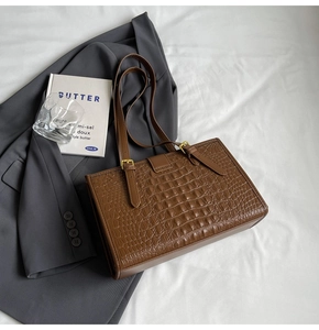Close-up of brown crocodile pattern texture and adjustable metal buckle on tote bag