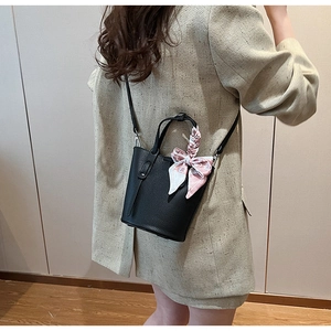 Detail of black pebbled leather bucket bag with decorative pink floral scarf on handle