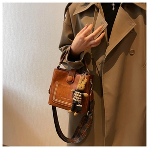 Macro detail of caramel bucket bag with metallic rivets and embroidered wide strap