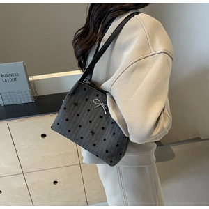 Detail of grey polka dot bucket bag with silver bow charm worn by a model in soft light