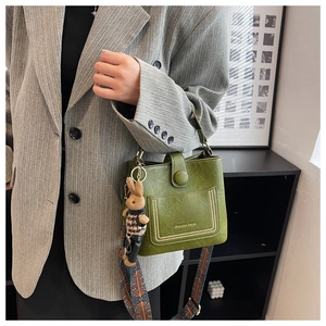 Detail of green leather bucket bag with tribal strap and rabbit charm on grey blazer