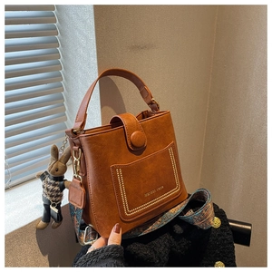 Brown vintage bucket bag with patterned strap and bunny pendant on black tweed