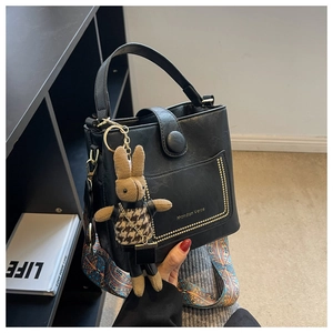 Detail of black bucket bag featuring golden logo, woven strap and plush rabbit charm