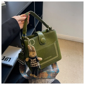 Detail of dark green bucket bag with metal rivets, printed strap, and rabbit pendant charm