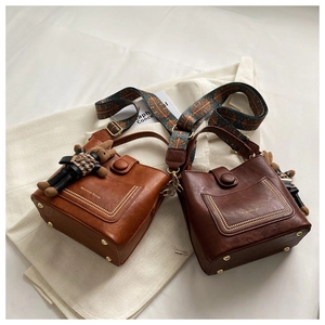 Detail of vintage bucket bags in brown PU leather with decorative wide strap and teddy charm