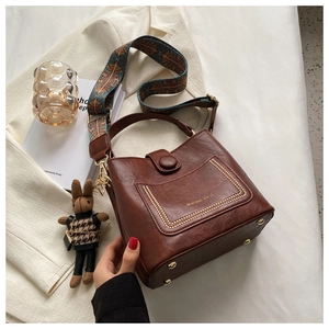 Detail of dark brown leather bucket bag with woven strap and rabbit charm accessory