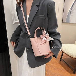 Pink lychee leather bucket bag with silk scarf handle, worn by model in gray suit