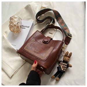 Detail of vintage brown leather bucket bag with gold rivets and ethnic print strap