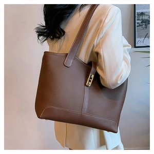 Close-up of a dark brown litchi grain leather tote bag with gold metal buckle detail