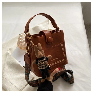 Brown bucket bag detail showing geometric wide strap and cute rabbit pendant charm