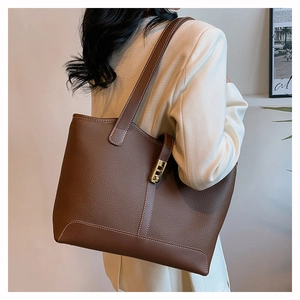Detail of brown litchi leather tote bag with white stitching and gold metal clasp