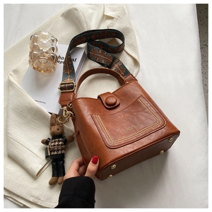 Detail of brown leather bucket bag with totem strap, gold studs and rabbit charm