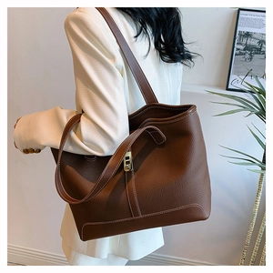 Detail of brown lychee texture tote bag with white stitching and gold clasp shown on model