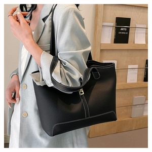 Close-up of black litchi grain leather tote bag with white contrast stitching details