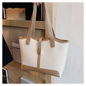 Detail of two-tone faux leather tote bag with gold hardware on a wooden stand