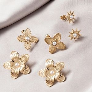 Macro detail of gold flower stud earrings with pearls on elegant grey silk background