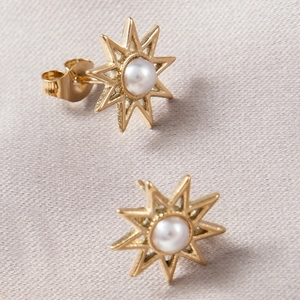 Detailed close-up of golden sunburst stud earrings with white pearl inlay on purple silk