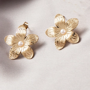 Exaggerated golden flower stud earrings with central pearl on soft silk fabric
