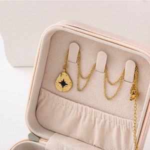 Détail du pendentif goutte doré avec étoile noire dans un écrin à bijoux rose