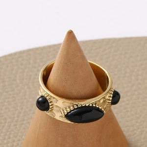 Détail macro d'une bague large dorée avec pierres naturelles noires sur support bois