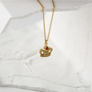 Elegant gold crown pendant necklace with a bright red stone on a white stone background