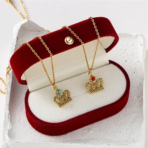 Elegant gold crown necklaces with blue and red gemstones in a red velvet jewelry box