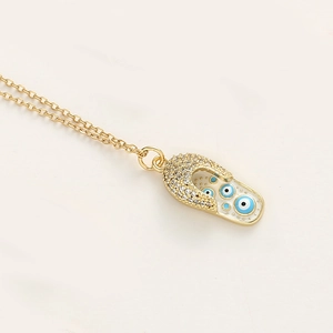 Détail du pendentif tong dorée avec cristaux étincelants et motifs émaillés œil grec