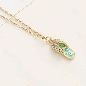 Détail du collier doré avec pendentif chaussure en émail vert et œil porte-bonheur