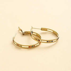 Détail de boucles d'oreilles créoles dorées avec rayures ajourées et pierres colorées