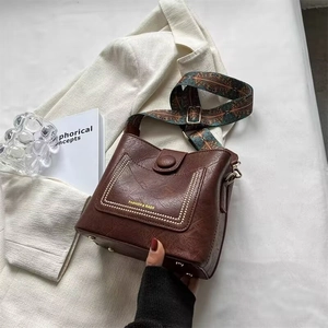 Retro brown leather bucket bag with ethnic woven strap on a white suit jacket