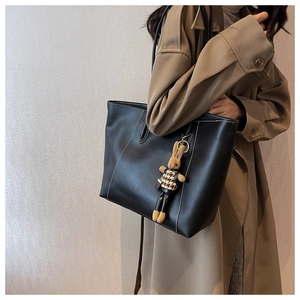 Détail du sac cabas noir avec surpiqûres blanches et charme de lapin sur un trench-coat