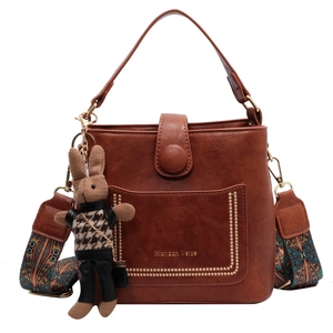 Brown bucket bag with woven strap, gold studs, and a small rabbit charm on white background