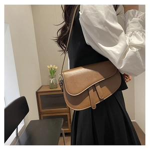 Detailed view of a brown matte leather saddle bag worn by a model in a warm setting