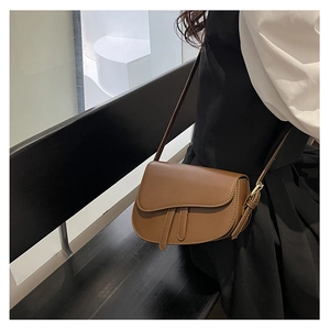 Close-up of a brown synthetic leather saddle bag with vintage buckle straps on a model