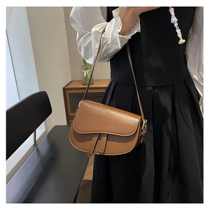 Close-up of a vintage brown leather saddle bag with decorative straps and slim shoulder strap