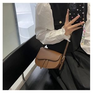 Brown matte leather saddle bag worn crossbody with adjustable strap and buckle details