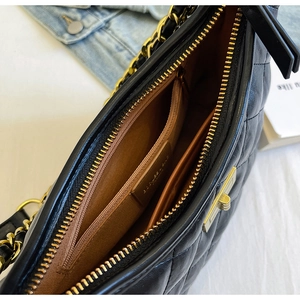 Macro view of black quilted chain bag featuring gold hardware and inner zipper pocket