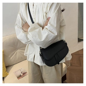 Detailed view of a black matte leather saddle bag with long straps worn on shoulder