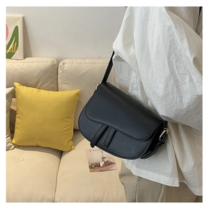 Detail of a black leather saddle bag with gold hardware worn as a crossbody bag