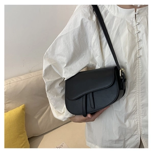 Model wearing a black matte leather saddle bag with golden hardware and adjustable strap