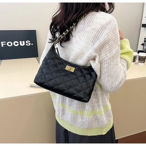 Detail of black quilted shoulder bag with gold twist lock and metal chain strap worn by model