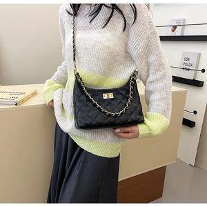 Detail of black quilted chain bag with gold metal lock and leather shoulder strap
