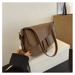 Detail view of dark brown saddle bag with gold buckles on a white display stand