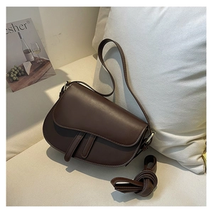 Detail of a dark brown saddle bag with adjustable strap on a minimalist white sofa