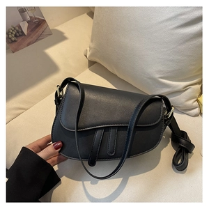 Detail of a black vintage saddle bag with decorative straps on a soft beige sofa