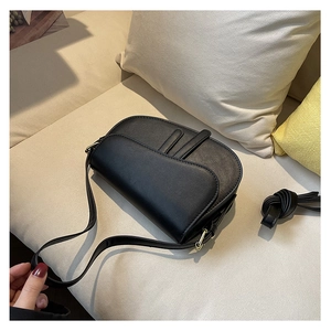 Detail of a matte black leather saddle bag with golden hardware on a soft sofa