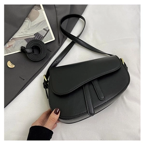 Detail of a black textured saddle bag with decorative straps on a stylish flat lay setup