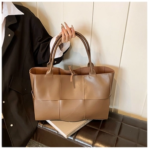 Lifestyle shot of woman holding large brown woven leather tote bag for work and commute