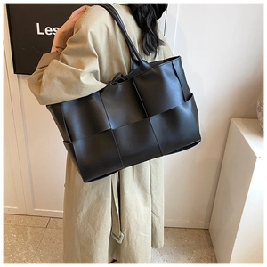 Detail of a black woven tote bag made with wide Intrecciato leather on a trench coat model